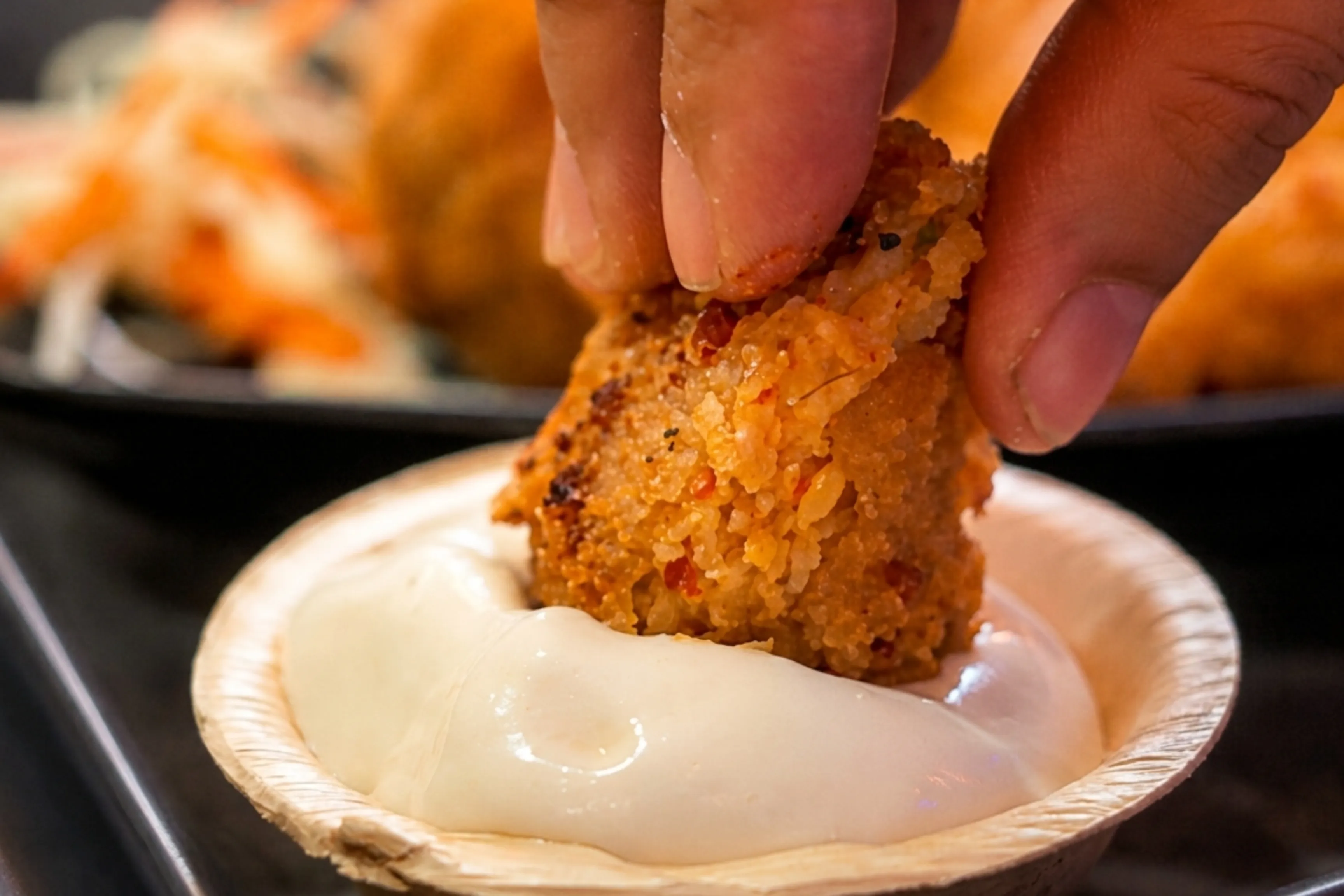 Hand dipping crispy cheese ball into creamy sauce at Game Xtreme